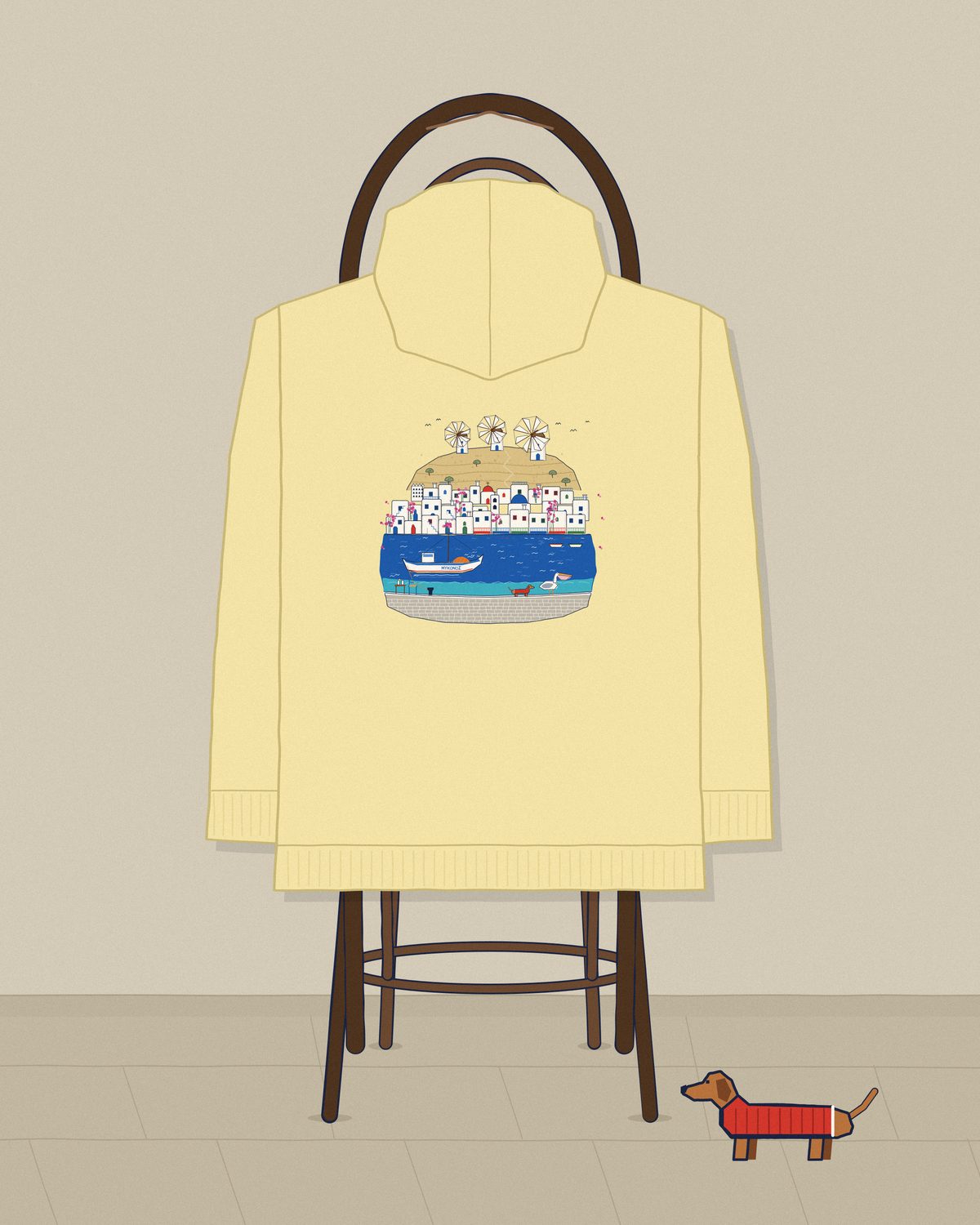 The butter Mykonos hoodie over a café chair, the dachshund beside it.